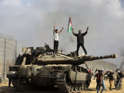 Жители Газы стоят на подбитом израильском танке у сломанного забора на границе, 7 октября 2023 года. Фото:Yousef Masoud / AP Photo